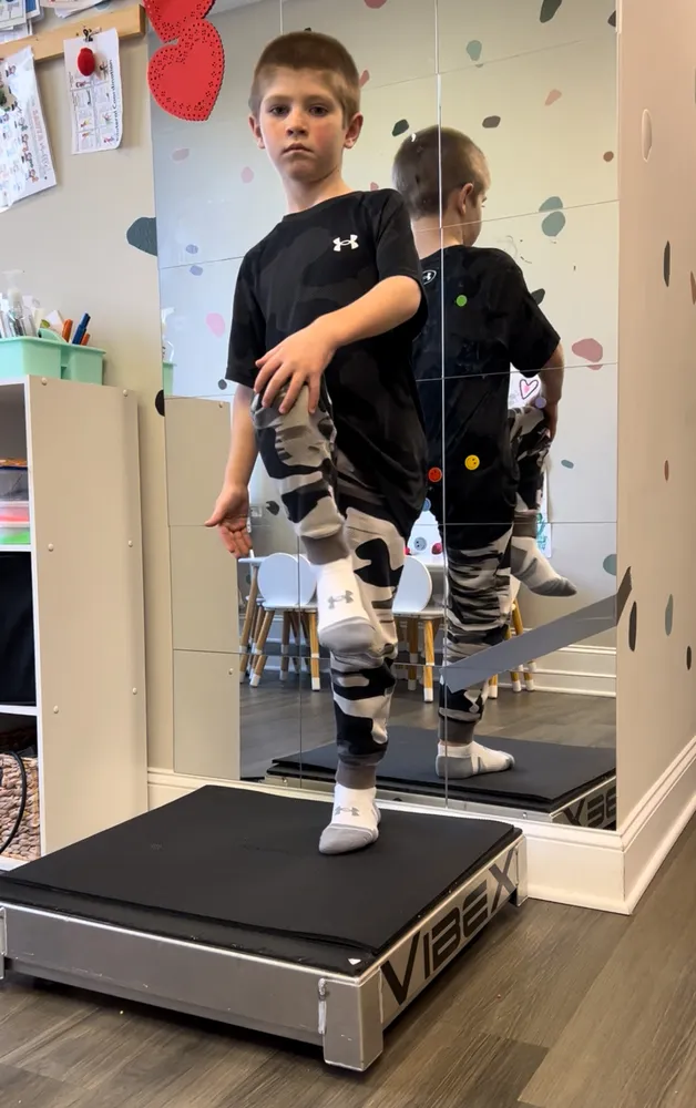 Child balancing on a platform in front of a mirror during physical therapy