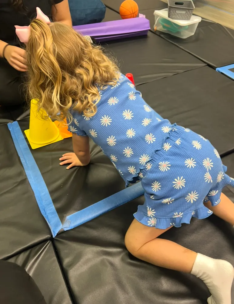 Child crawling along a taped pathway on gym mats during motor therapy