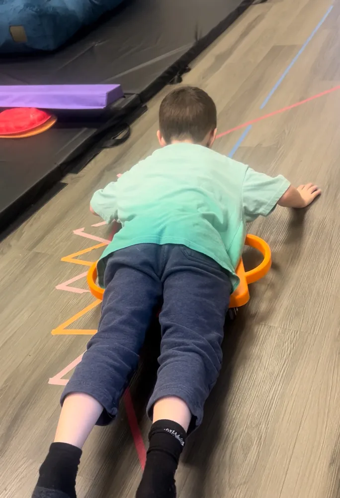 Child on a scooter board following a taped floor path