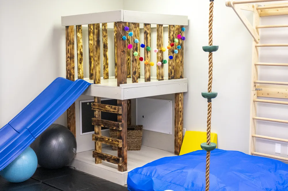 Sensory gym with a wooden climbing loft, blue slide, and crash pads at Integrative Wellness and Therapeutics in Cornelius, NC
